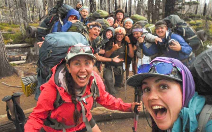 a group of outward bound students carrying backpacks pose excitedly for a photo